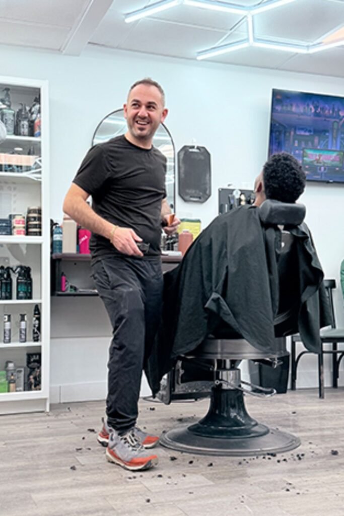 John A Barbershop a barberf with a man in the barber chair. The barber is similing at the camera