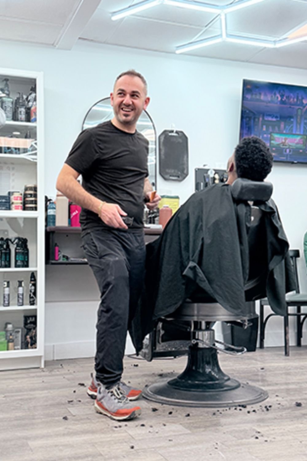 John A Barbershop a barberf with a man in the barber chair. The barber is similing at the camera